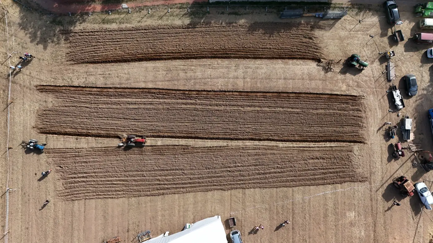 Vue aérienne du labour à l’ancienne : trois bandes labourées et matériel d’époque en bordure de parcelle